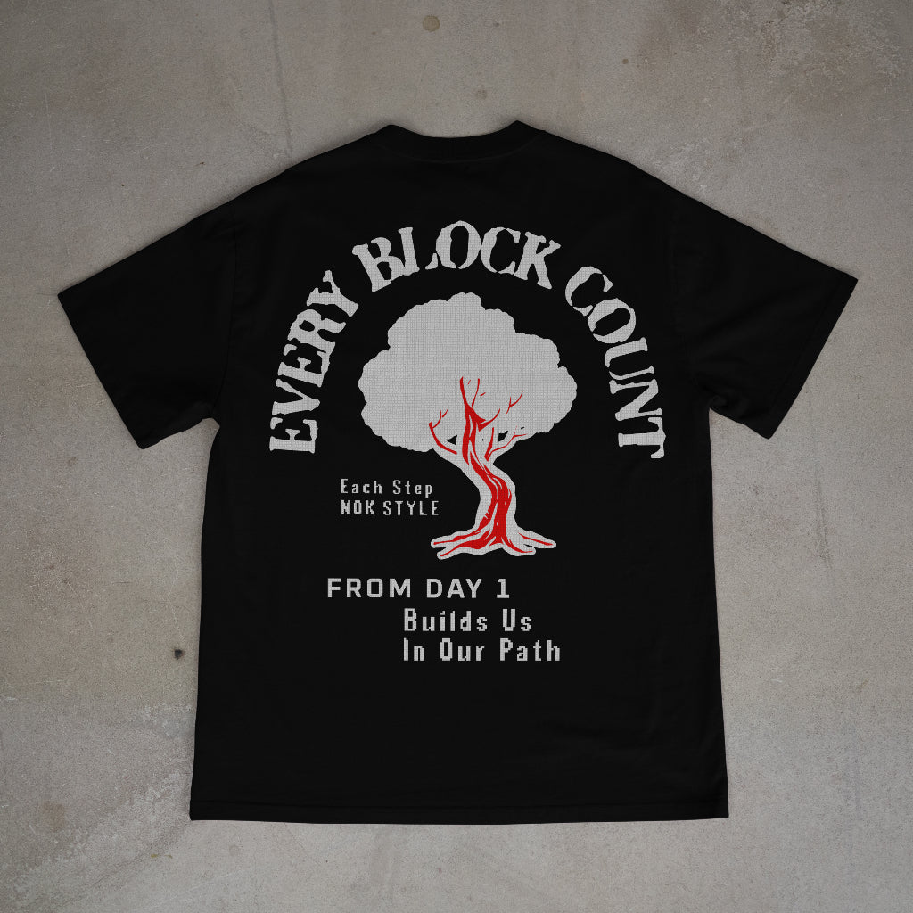 Flat back mockup of the Every Block Count black t-shirt with detailed tree graphic and text, emphasizing the 'From Day 1' message.