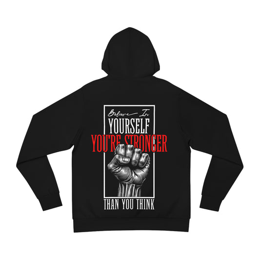 Flat lay of a black hoodie featuring a bold back design with a raised fist graphic and empowering text reading 'Believe in Yourself, You're Stronger Than You Think'.