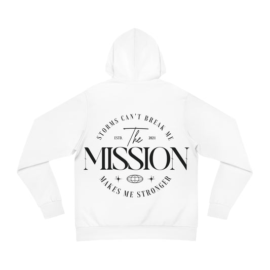 Flat lay of a white hoodie with bold typography on the back reading 'Storms Can’t Break Me. Makes Me Stronger. The Mission.