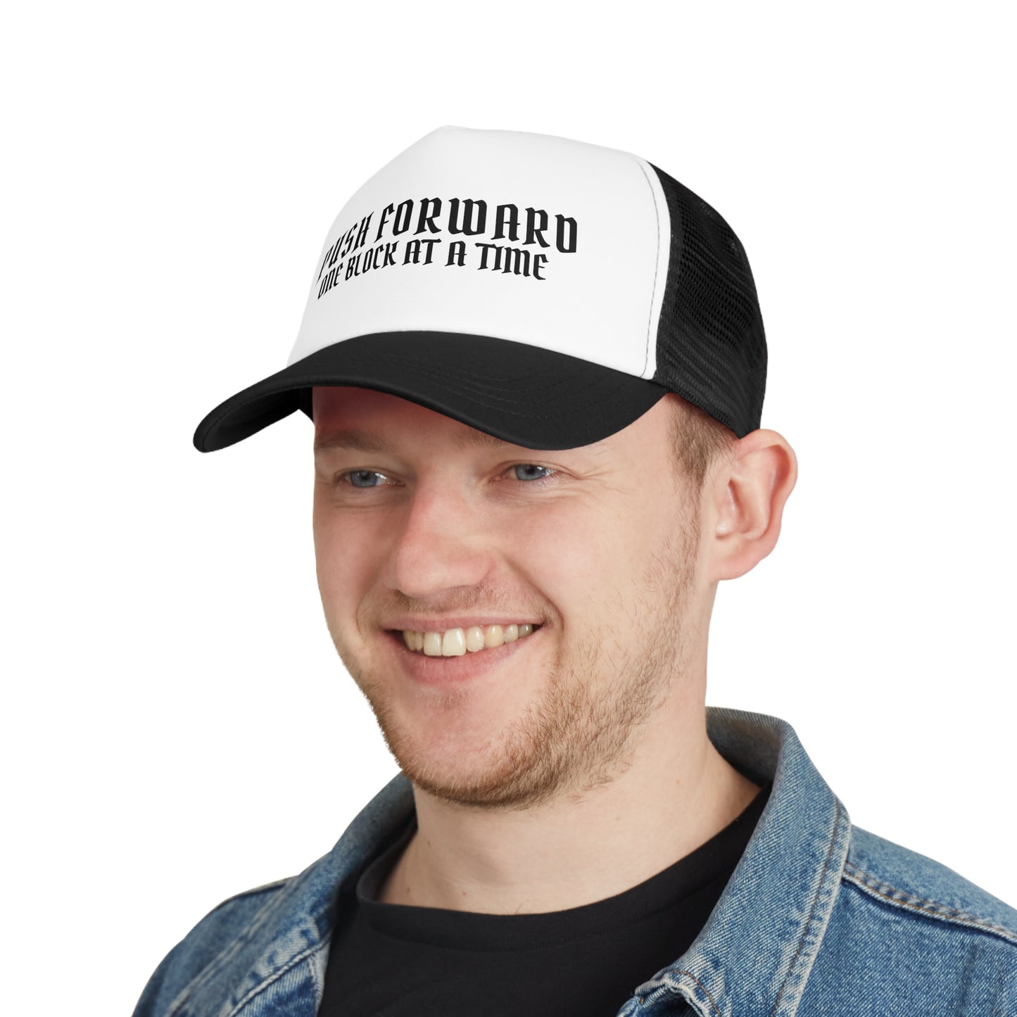 Man wearing a black and white trucker cap with the text 'Push Forward, One Block at a Time' printed on the front. The cap features a structured fit and a curved bill.