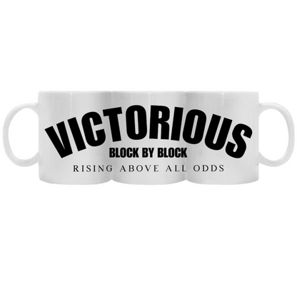 A sleek white ceramic mug with the full wrap design featuring bold "Victorious" text and the tagline "Block by Block - Rising Above All Odds" in black typography.